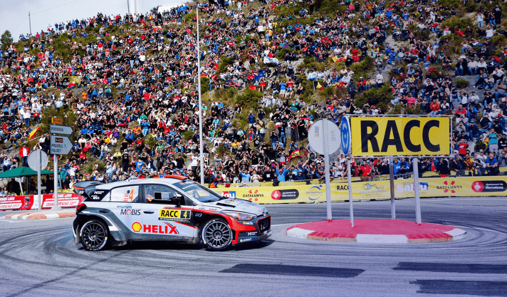 Hyundai i20 WRC rally car cornering in front of a large crowd at Rally Catalunya.