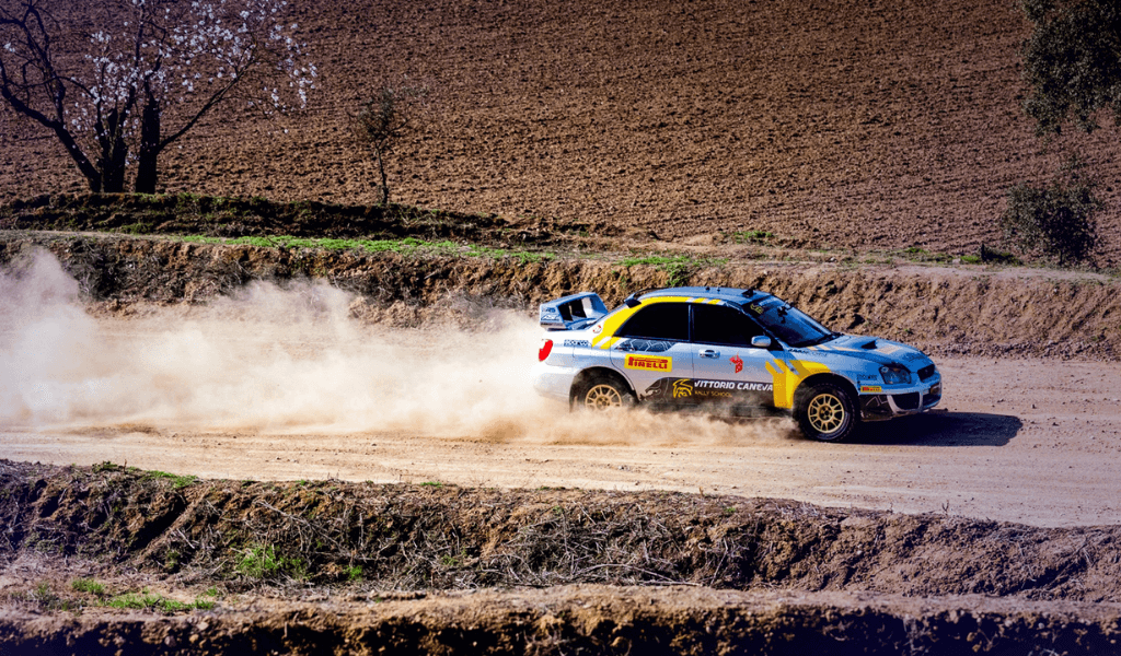 Rally car kicking up dust while driving on a dirt track in a field.