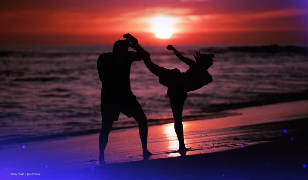 Silhouette sparring scene with two people practicing martial arts on the beach at sunset.