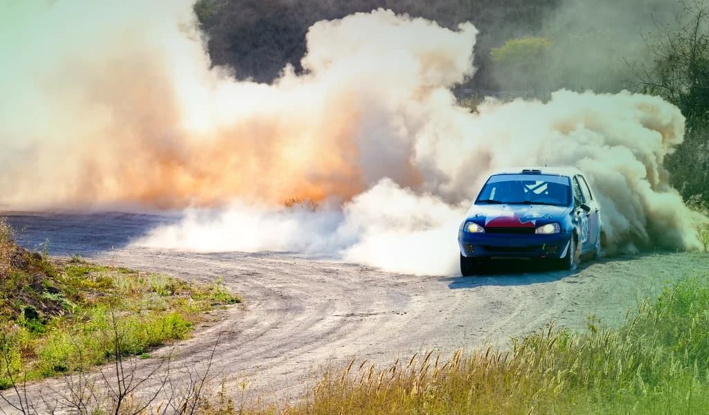 Rally car sliding through a dirt corner with a large cloud of dust trailing behind.