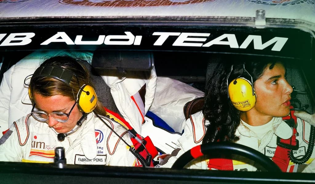 Michèle Mouton and co-driver Fabrizia Pons wearing headsets inside an Audi rally car during a stage race.