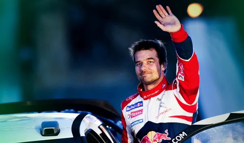 Sébastien Loeb waving beside his Citroën rally car in a racing suit.
