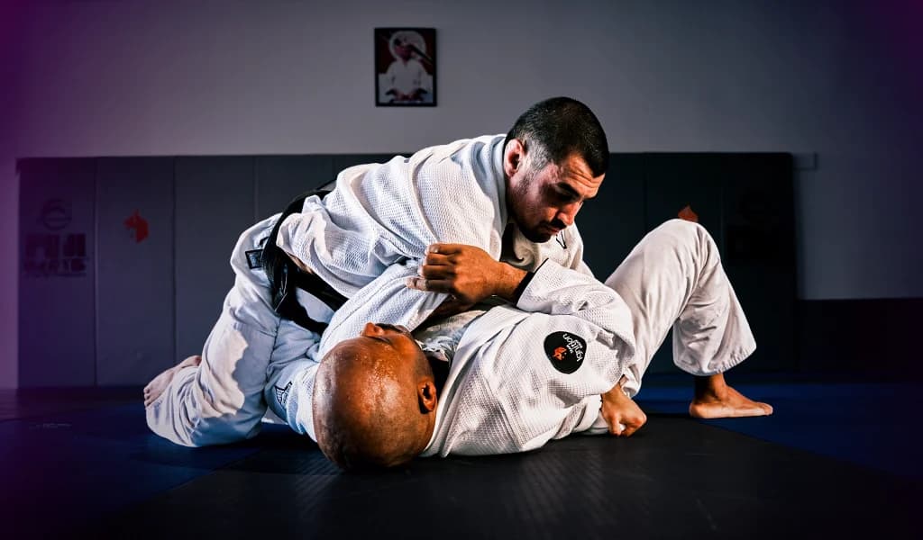 Kron Gracie and Selema Masekela grappling on a mat in a training gym wearing white Gis.