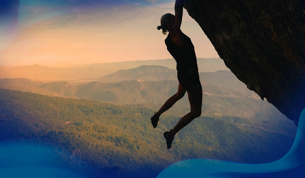 Silhouette of Alex Johnson hanging from a rock face during a challenging climb, with a stunning mountain landscape in the background at sunset.