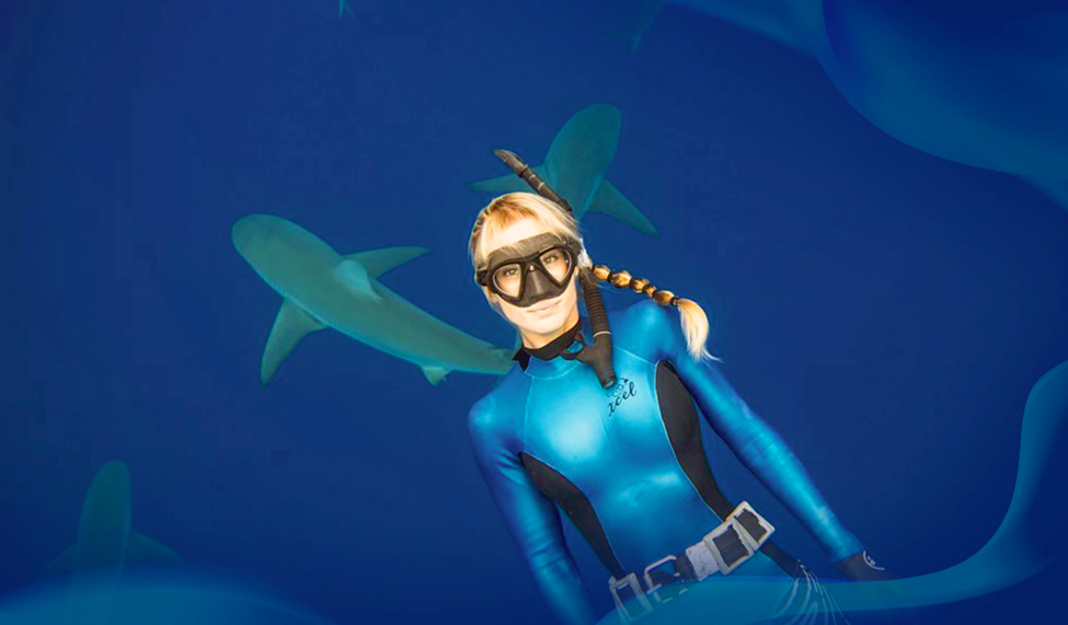 Ocean Ramsey swimming underwater with sharks, wearing a blue wetsuit and snorkeling gear.