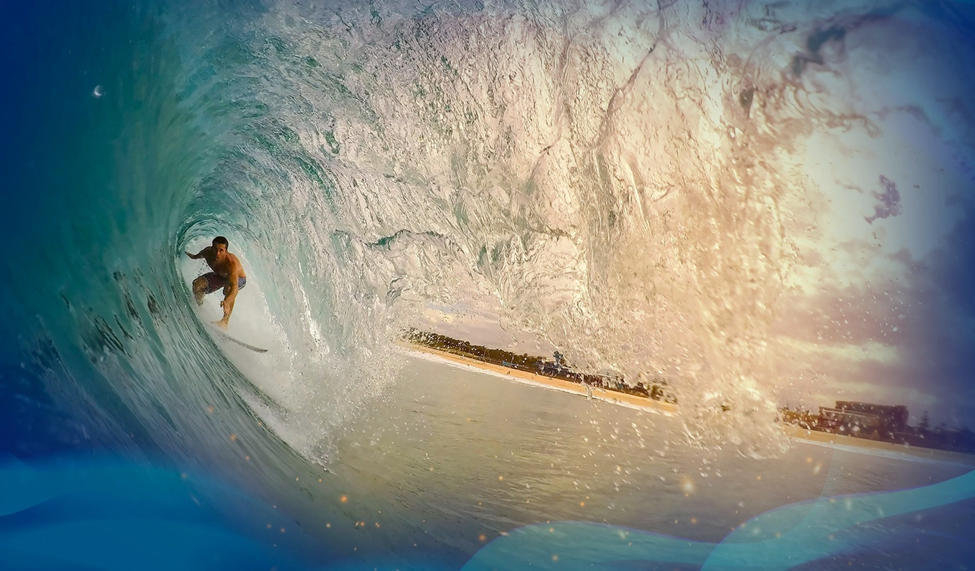 Surfer inside a wave tube, with sunlight shining through and the shoreline in the background.