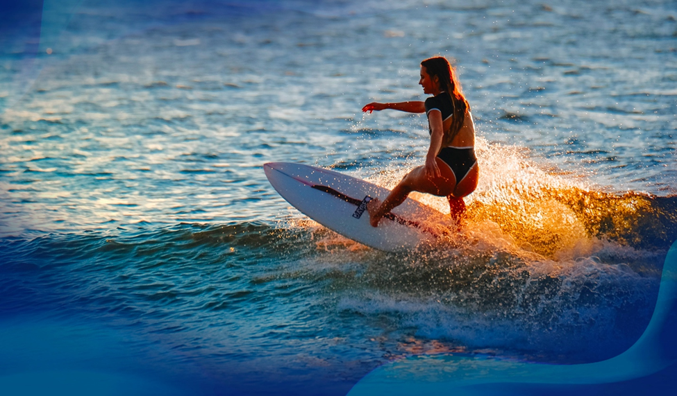 Alana Blanchard riding a wave during sunset, with water splashing as she maneuvers her surfboard.