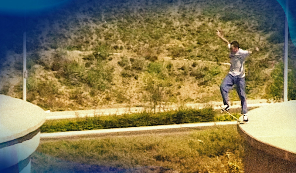 A skateboarder in mid-air, ollieing between two large water towers, with a desert landscape in the background.