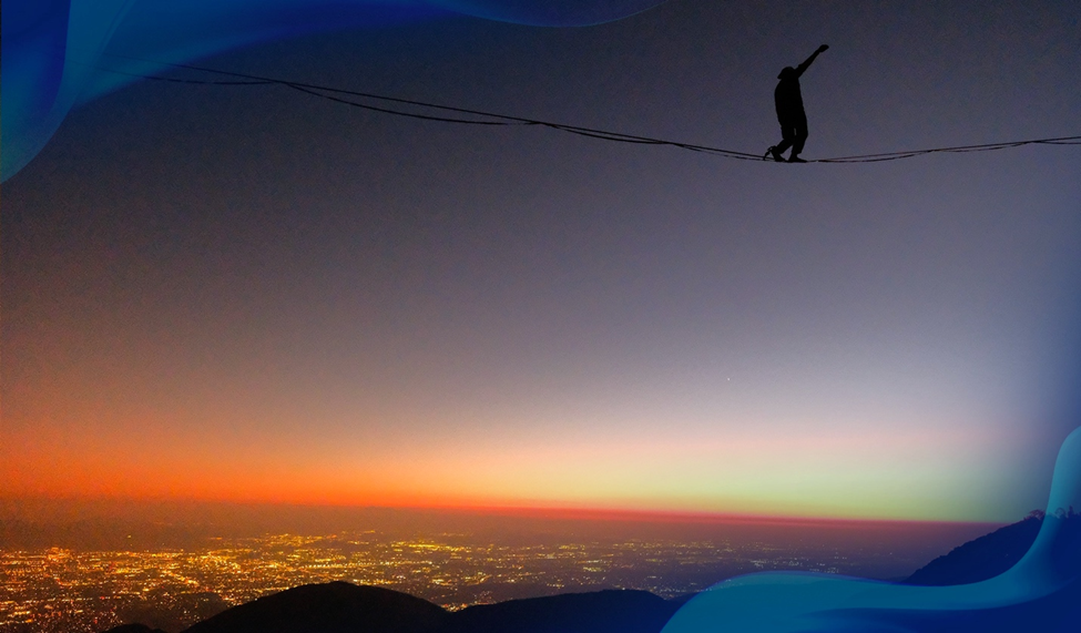 A silhouette of Ryan Robinson walking across a highline midair. Below him is a sunset on the horizon and the lights of a distant cityscape.