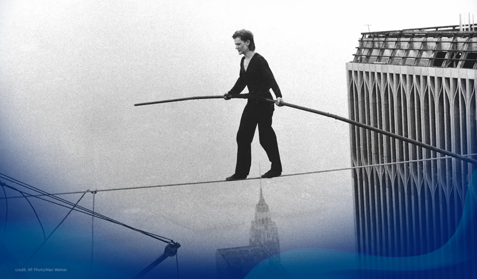 Philippe Petit performs a highwire walk between the Twin Towers, holding a balancing rod with the Empire State Building below.