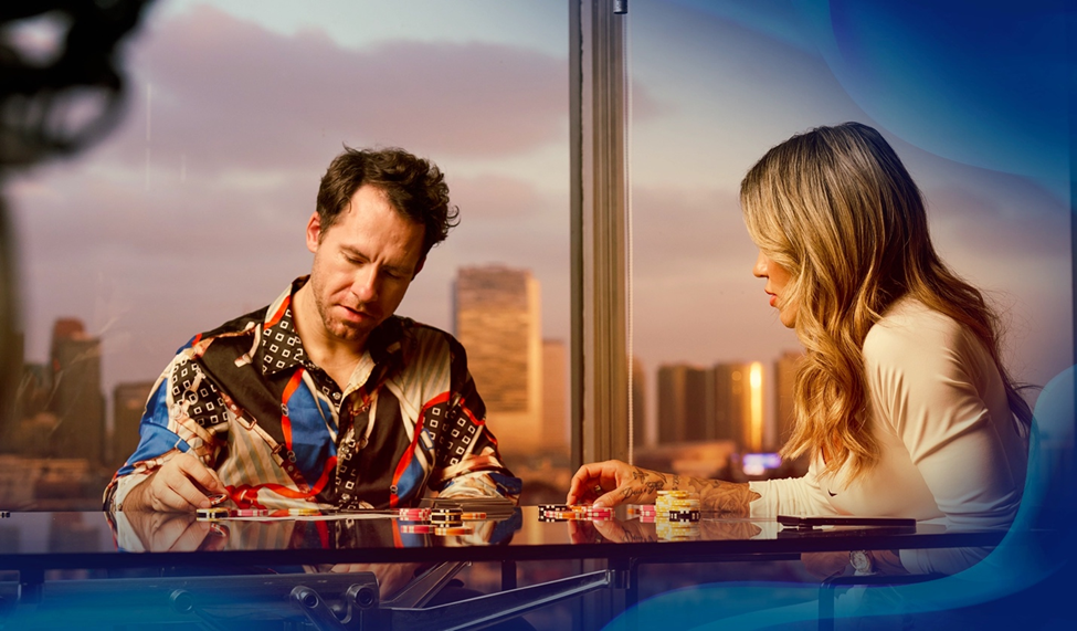 Daniel Cates and Leticia sit across a poker table stacked with chips, intently focused on the game. A cityscape view is visible through large windows.