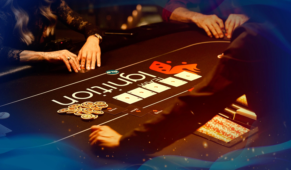 Close-up of players’ hands on a poker table with stacks of poker chips, a deck of cards, and the Ignition logo in view.