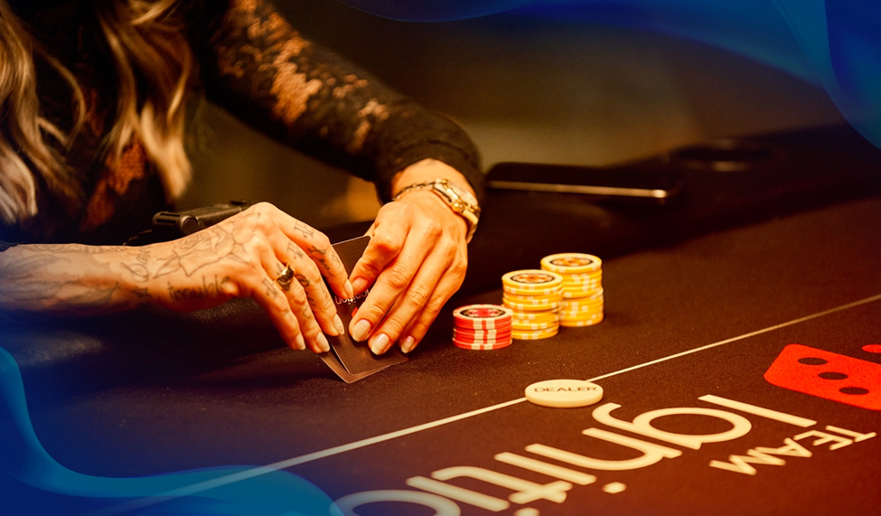 A player in a black lace outfit reaches for cards on a poker table stacked with yellow and red poker chips.