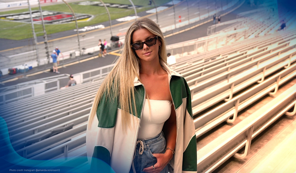 Amanda Sorenson smiling and wearing sunglasses, standing in the bleachers of a race track with a green and white jacket and casual attire