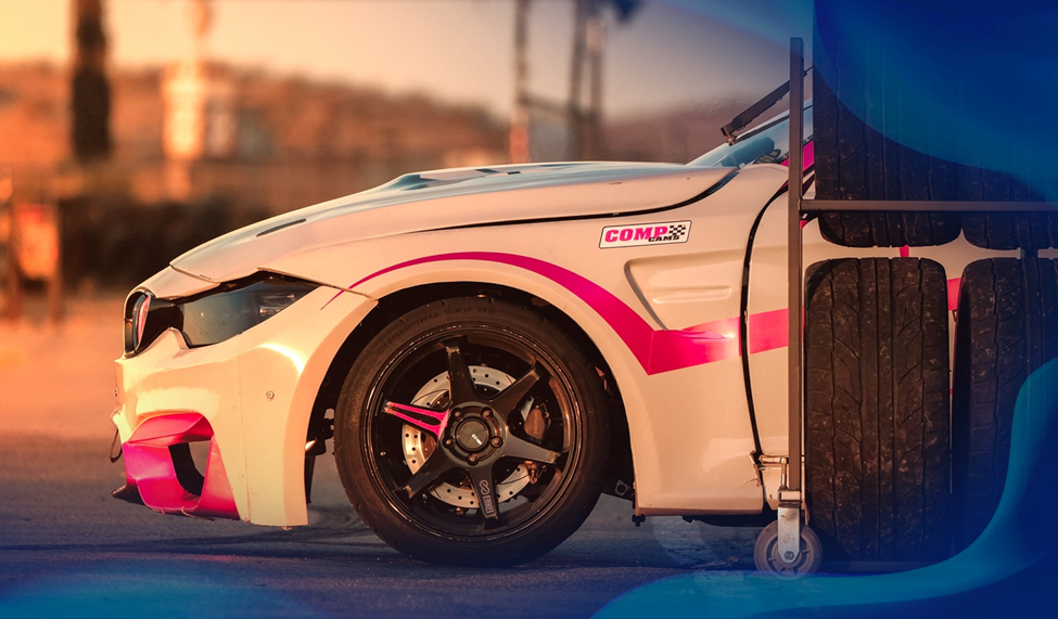 Close-up of a white drift car with its side profile featuring a pink accent stripe and stacked tires in the foreground.