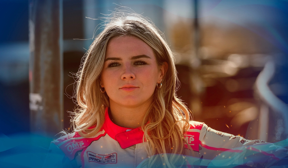 Close-up portrait of Amanda Sorenson in a racing suit, standing confidently outdoors with sunlight highlighting her hair.