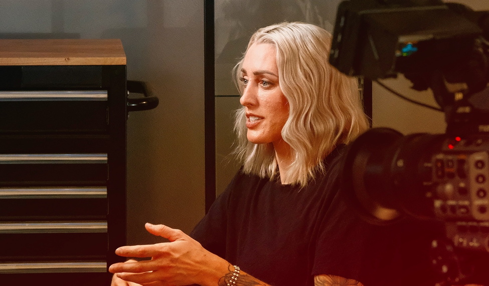 Alex Johnson sits during an interview, gesturing while talking. She is in a workshop setting, with a camera capturing the moment.